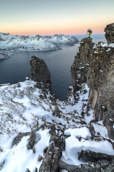 Photographer on the rocks on top of Mount Hesten admires the Mefjorden and the frozen sea at sunrise Senja Tromsø Norway Europe