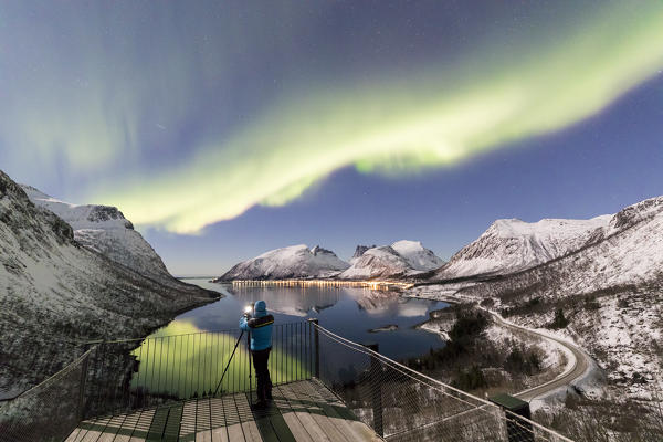 Photographer on platform admires the Northern lights and stars reflected in the cold sea Bergsbotn Senja Tromsø Norway Europe