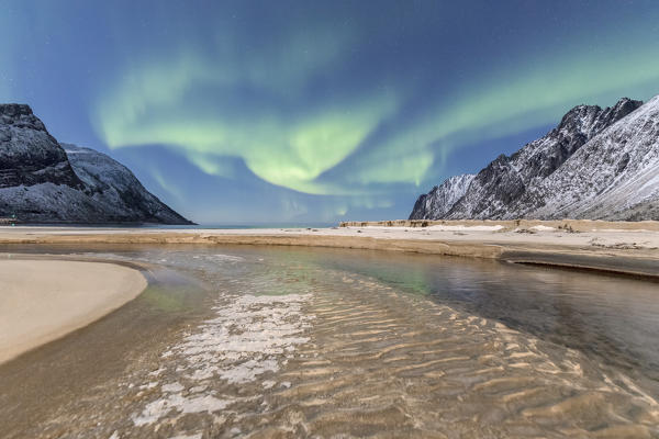 Green lights of Aurora Borealis reflected in the cold sea surrounded by snowy peaks Ersfjord Senja Tromsø Norway Europe