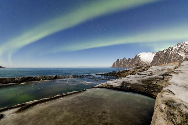 The Northern Lights and stars illuminate the rocky peaks and icy sea Tungeneset Senja Tromsø Norway Europe