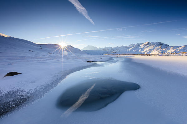 Rays of sun on the frozen Lake Piz Umbrail framed by Mount Ortles in background Braulio Valley Valtellina Lombardy Italy Europe