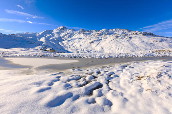 Blue sky and sun on Lake Piz Umbrail surrounded by snowy peaks at Stelvio Pass Braulio Valley Valtellina Lombardy Italy Europe