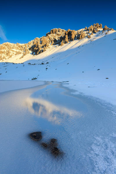 Snowy peaks are reflected in the icy Lake Piz Umbrail at dawn Braulio Valley Valtellina Lombardy Italy Europe