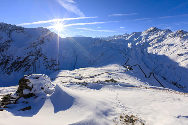 Sunbeams at dawn on the snowy landscape and the hairpin turns of Stelvio Pass Braulio Valley Valtellina Lombardy Italy Europe