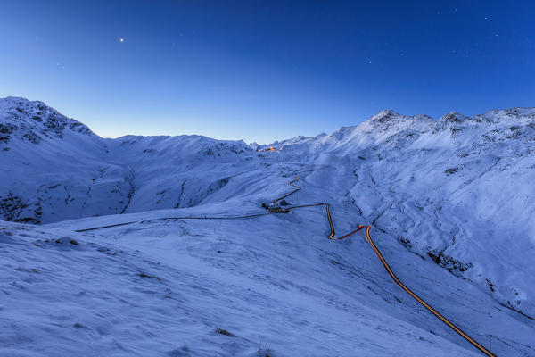 Blue light of dusk on the snowy landscape and the hairpin turns of Stelvio Pass Braulio Valley Valtellina Lombardy Italy Europe