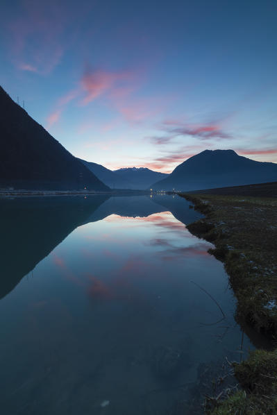 Pink sky at sunset reflected in the calm water of Adda river Sirta Forcola province of Sondrio Valtellina Lombardy Italy Europe