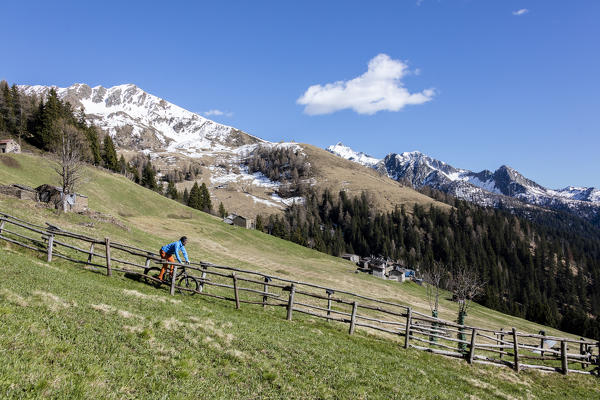 Mountain bike on green meadows framed by snowy peaks in spring Albaredo Valley Orobie Alps Valtellina Lombardy Italy Europe