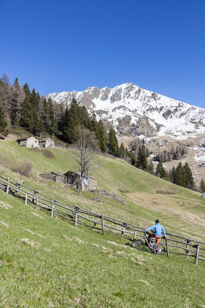 Mountain bike on green meadows framed by snowy peaks in spring Albaredo Valley Orobie Alps Valtellina Lombardy Italy Europe