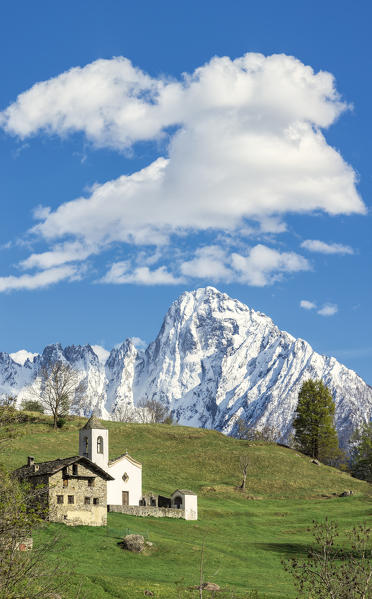 Panorama of church and meadows framed by snowy peak of Pizzo di Prata Daloo Chiavenna Valley Valtellina Lombardy Italy Europe