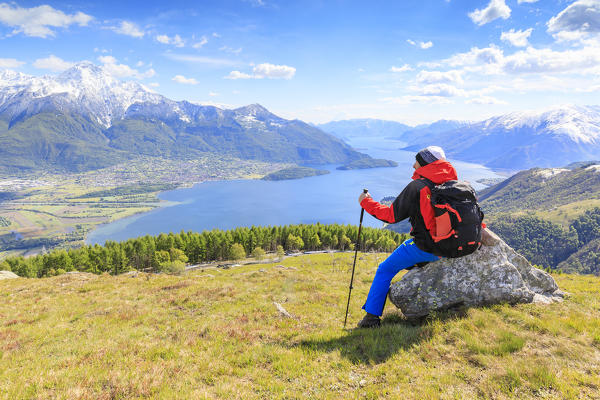 Hiker on green meadows admires Lake Como framed by snowy peaks Montemezzo Alpe Zocca Lombardy Italy Europe