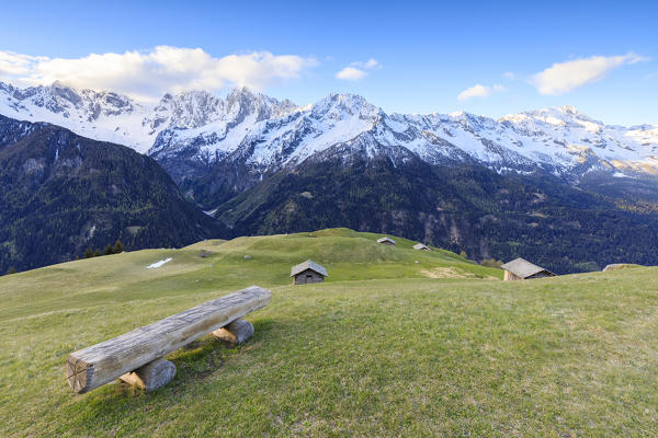 Meadows and wooden huts framed by snowy peaks at dawn Tombal Soglio Bregaglia Valley canton of Graubünden Switzerland Europe