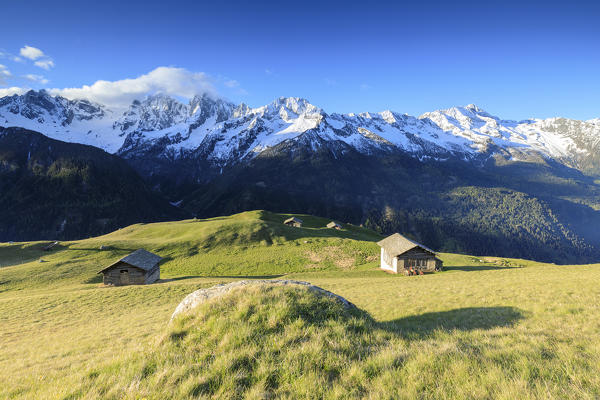 Meadows and wooden huts framed by snowy peaks in spring Tombal Soglio Bregaglia Valley canton of Graubünden Switzerland Europe
