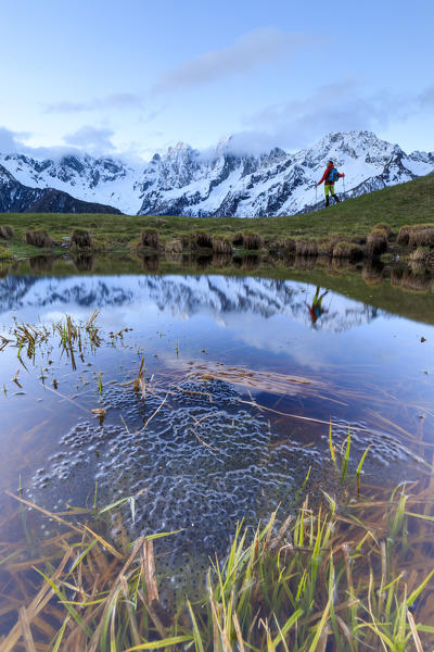 Hiker framed by snowy peaks reflected in water at dawn Tombal Soglio Bregaglia Valley canton of Graubünden Switzerland Europe