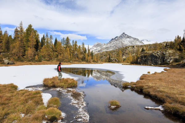 Hiker admires Sasso Moro reflected in the icy Lake Mufulè Malenco Valley Lombardy province of Sondrio Valtellina Italy Europe