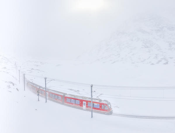 Bernina Express train at Bernina Pass during a snowstorm, canton of Graubünden, Engadin Valley, Switzerland