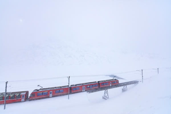 Bernina Express train at Bernina Pass during a snowstorm, canton of Graubünden, Engadin Valley, Switzerland