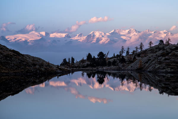 The majestic glaciers in the Mount Rosa range reflecting in the water of Lake Bianco at sunset. Mont Avic natural park. Aosta Valley. Italy Europe