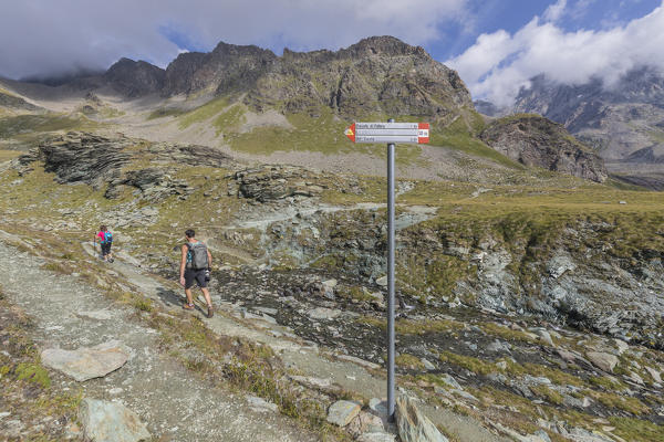 Hikers proceed on path Sentiero Glaciologico of Fellaria Glacier, Malenco Valley, Valtellina, Lombardy, Italy