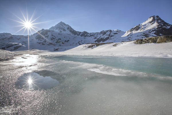 A double sun reflecting in a pool during the vernal thaw at the Lake Bianco - Gavia pass, Alps, Valtellina, Sondrio, Lombardy, Italy. EUrope