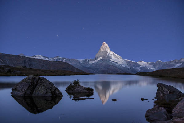 The Matterhorn colossus reflecting in the still water of Lake Stellisee in a clear night. This mirror is just one of the many little lakes spotting the Zermatt heights, famous Swiss resort - Zermatt, Canton of Valais, Switzerland. Europe