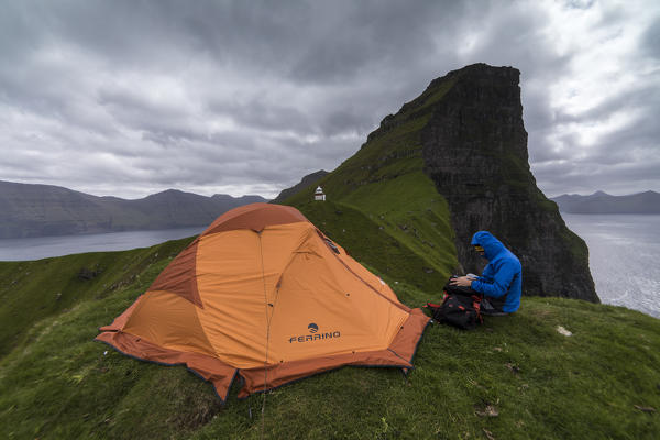 Hiker and tent on cliffs around Kallur Lighthouse, Kalsoy island, Faroe Islands, Denmark