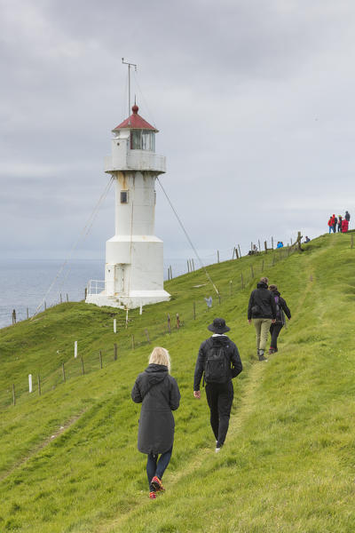 Hikers walks to the lighthouse on islet known as Mykines Holmur, Mykines island, Faroe Islands, Denmark