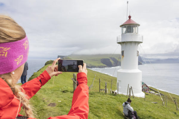 Tourist takes pictures of lighthouse on islet known as Mykines Holmur, Mykines island, Faroe Islands, Denmark