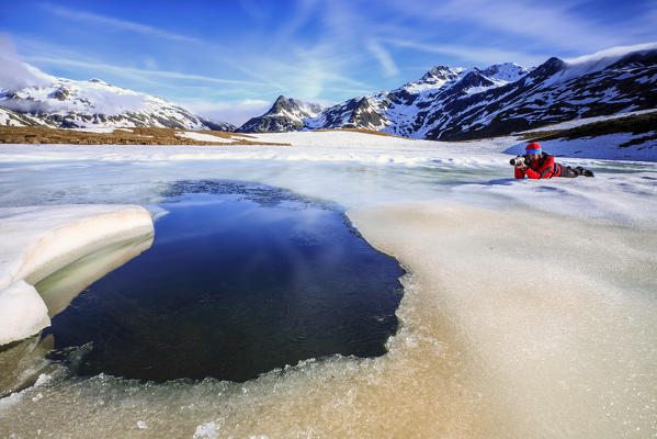 Photographer on ice at Lake Andossi during thaw, Chiavenna Valley, Spluga Valley, Sondrio province, Valtellina, Lombardy, Italy