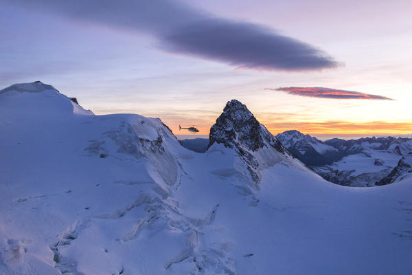 Helicopter in flight on snowy peak of Cresta Guzza towards Piz Bernina, Valmalenco, Lombardy, border of Italy and Switzerland