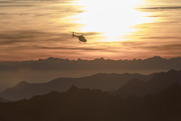 Aerial view of helicopter in flight towards Monti Lariani at sunset, Valmalenco, Val Masino, Valtellina, Lombardy, Italy