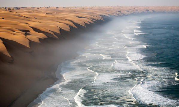 The waves of the Atlantic Ocean crashing against the sandy wall of the Namib desert. Namibia. Africa