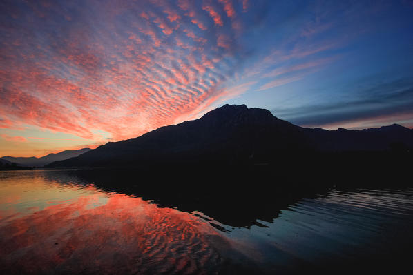 The Berlinghera silhouette and some colorful clouds during an amazing sunset are reflected in the Lake Mezzola Valchiavenna Valtellina Sondrio, Lombardy, Italy Europe