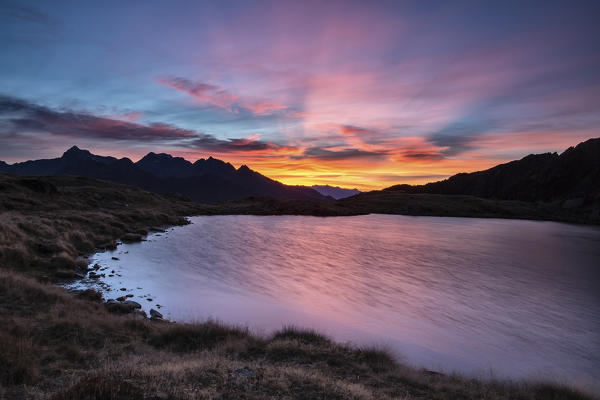 Amazing sunrise coloring the whole sky while the wind gently moves the surface of Lake Arcoglio - Valmalenco, Valtellina Sondrio, Lombardy, Italy Europe