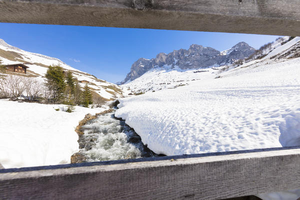 Torrent surrounded by snow seen from wooden fence, Partnun, Prattigau, Davos, canton of Graubunden, Switzerland