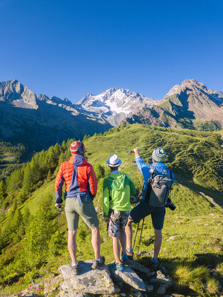 Hikers on rocks look towards Monte Disgrazia from Scermendone Alp, Sondrio province, Valtellina, Rhaetian Alps, Lombardy, Italy