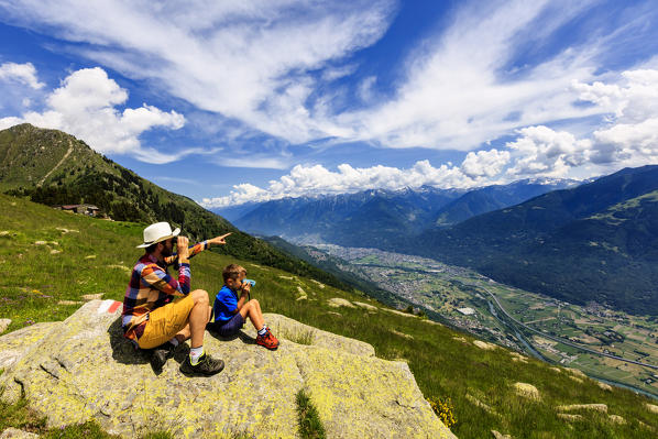 Father and son with binoculars look towards Morbegno from Alpe Bassetta, Valtellina, Sondrio, Lombardy, Italy