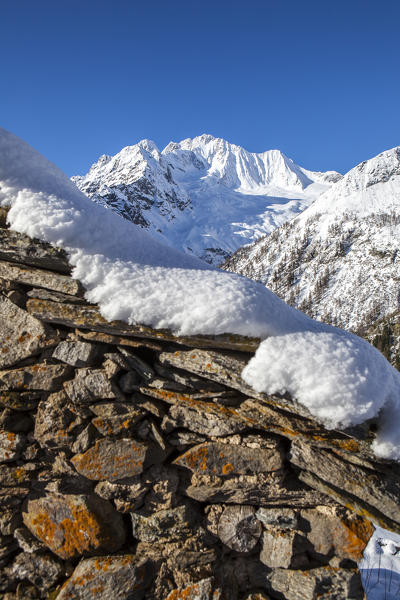 Stone hut covered with snow with Monte Disgrazia on background, Alpe dell'Oro, Valmalenco, Valtellina, Lombardy, Italy