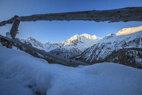 View of snowy Monte Vazzeda from wood fence, Alpe dell'Oro, Valmalenco, Valtellina, Sondrio province, Lombardy, Italy