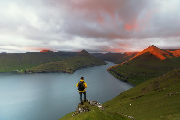 Hiker on top of rocks looks at the fjords, Funningur, Eysturoy island, Faroe Islands, Denmark