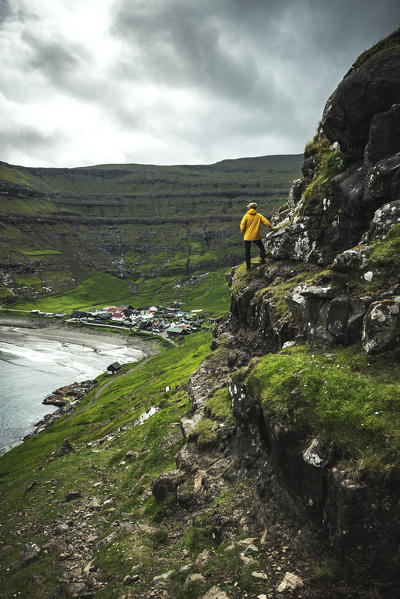 Man on cliffs looks towards the village of Tjornuvik, Streymoy island, Faroe Islands, Denmark