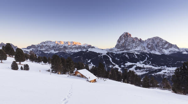a view of a beautiful winter sunset in Val Gardena with an alpine hut in foreground and the Sella Group and Langkofel in the background, Bolzano province, south Tyrol, Trentino Alto Adige, Italy