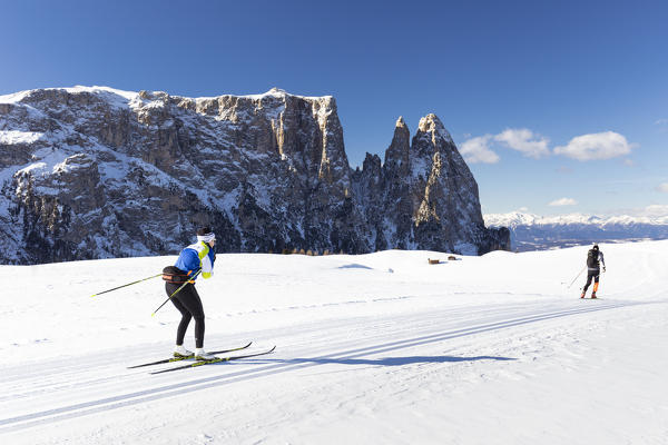 two athletes are running with cross-country skis on Seiser Alm with the Schlern in the background, Bolzano province, South Tyrol, Trentino Alto Adige, Italy