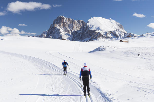 two athletes are running with cross-country skis on Seiser Alm with the Langkofel and Plattkofel in the background, Bolzano province, South Tyrol, Trentino Alto Adige, Italy