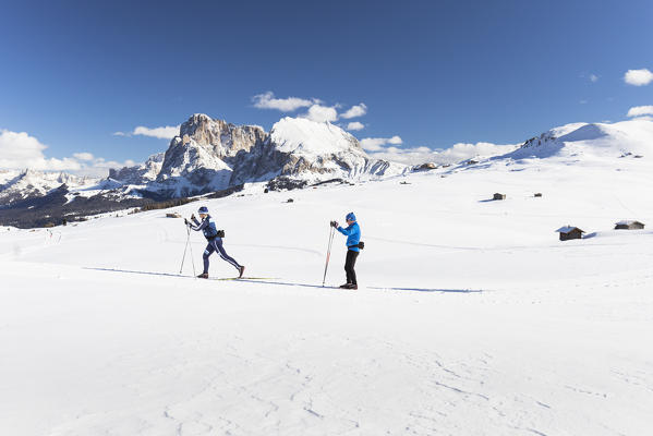 two athletes are running with cross-country skis on Seiser Alm with the Langkofel and Plattkofel in the background, Bolzano province, South Tyrol, Trentino Alto Adige, Italy