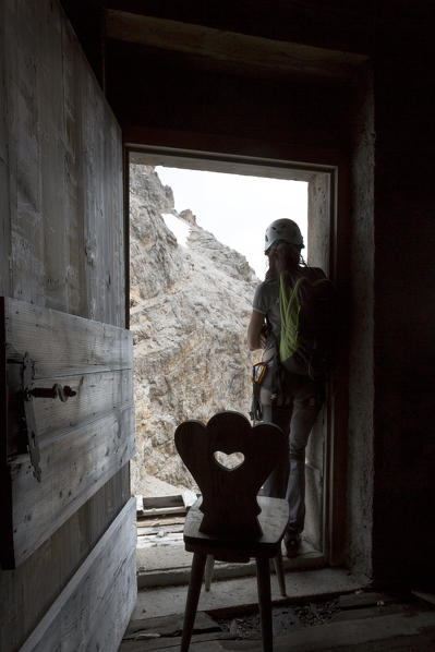 A climber stands at the door of a bivouac and looks towards the mountains, Belluno province, Veneto, Italy