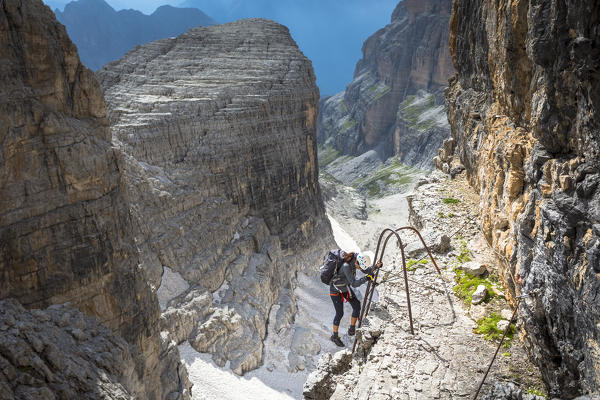A climber is getting down an iron ladder along the via ferrata in the Brenta Group, Trento province, Trentino Alto Adige, Italy