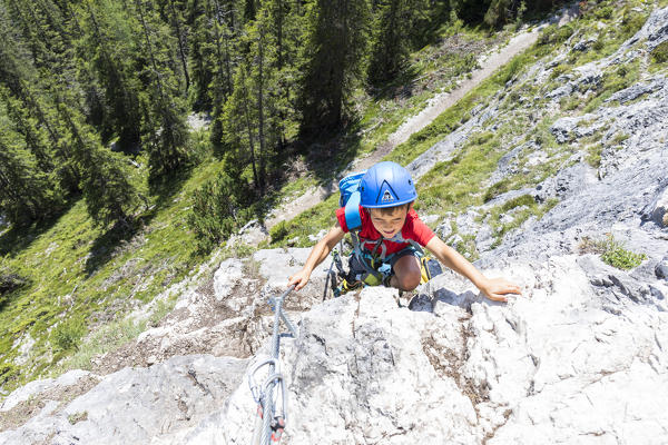 a kid climbing the via ferrata (iron path) Les Cordes in the Dolomites, Bolzano province, South Tyrol, Trentino Alto Adige, Italy