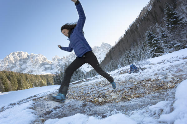 a joyful moment during a winter trekking while the model jumps the creek in Venegia Valley, Trento province, Trentino, Italy, Europe 