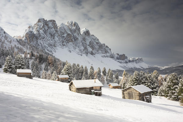 a winter view of the Puez Geisler Natural Park in Villnöss with some huts in foreground and the Geisler in the background, Bolzano province, South Tyrol, Trentino Alto Adige, Italy, Europe