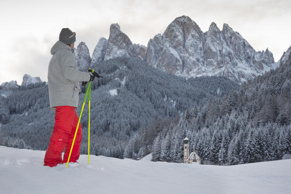a view of a winter trekking in Villnöss with one person looking to the church of S. John in Ranui and the Geisler in the background, Bolzano province, South Tyrol, Trentino Alto Adige, Italy, Europe